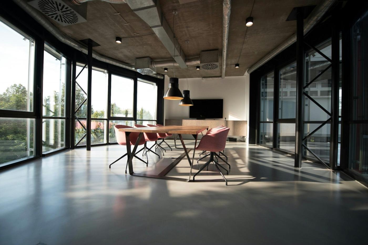 An empty meeting room with a long table and tall windows, set for a review.