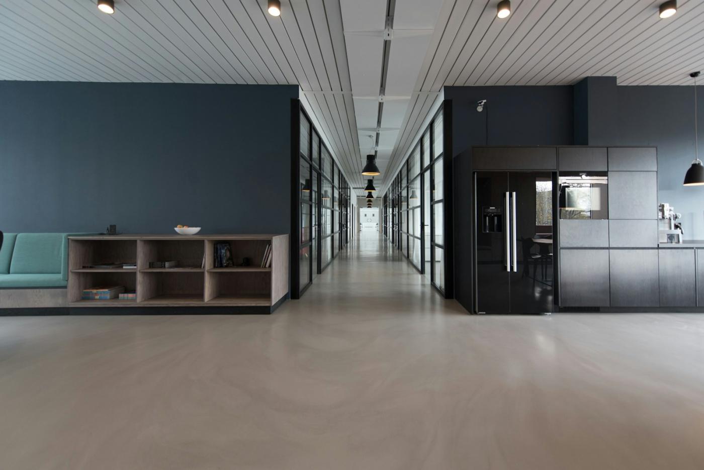 A workplace interior with a long corridor and glass-walled rooms.