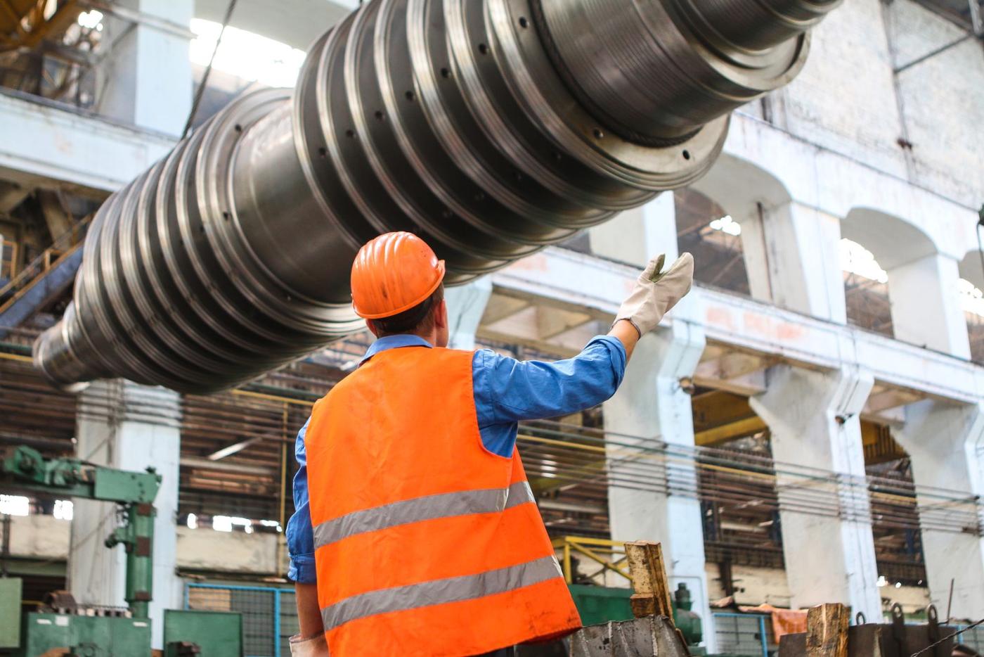 A technician guiding a large machined part through a plant bay.